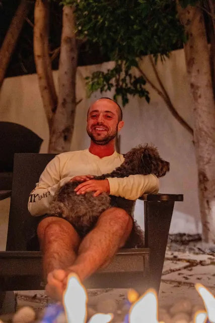 A man by a fire pit with his dog on his lap